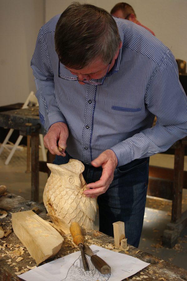 mężczyzna rzeźbiący sowę z drewna lipowego